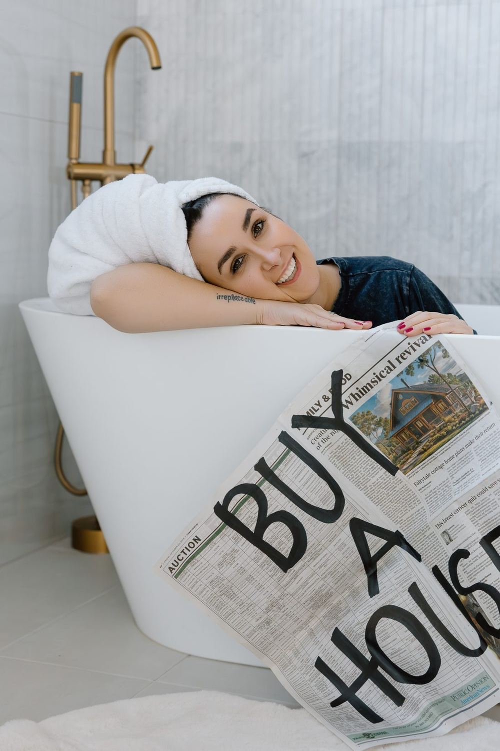 Lacie in a bathtub holding a newspaper that says Buy a House