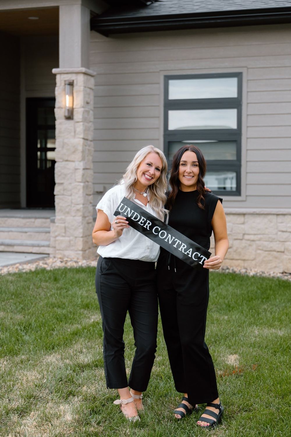 Lacie Packard and Sarah Bymers holding an Under Contract sign in a front yard